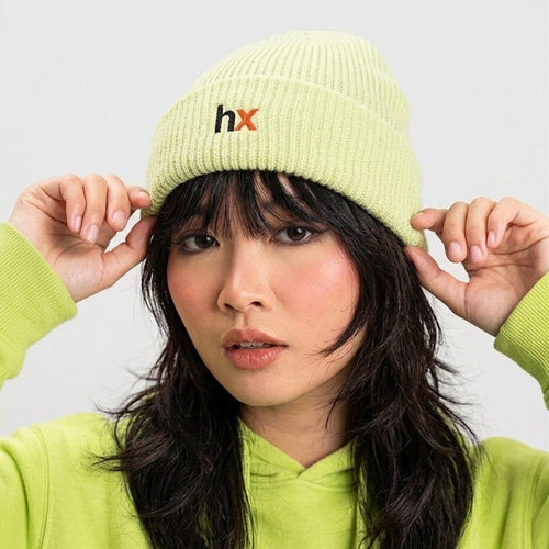 Person wearing a light green beanie with 'hx' logo and matching green hoodie against a white background